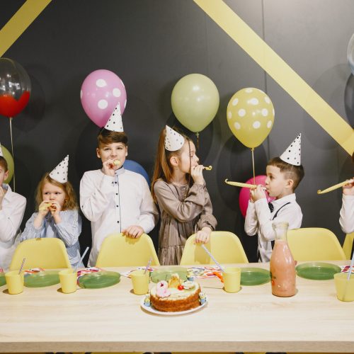 Children's funny birthday party in decorated room. Happy kids with cake and ballons.